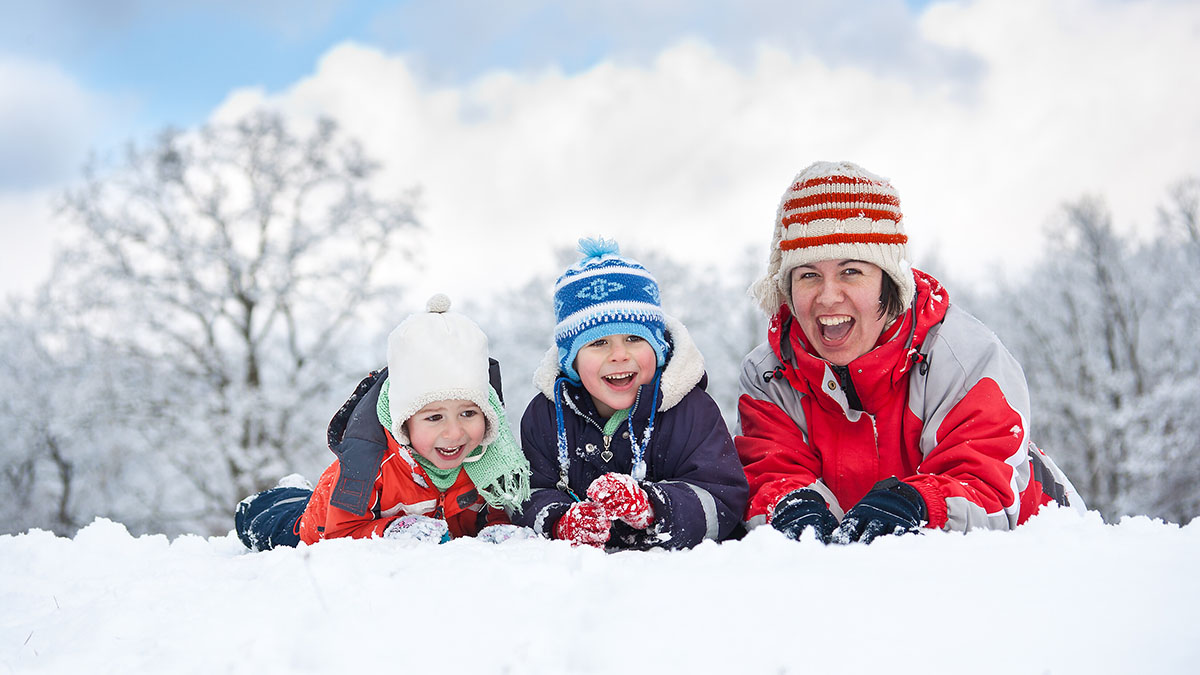 A mom and two children bundled in winter clothing smile in the snow