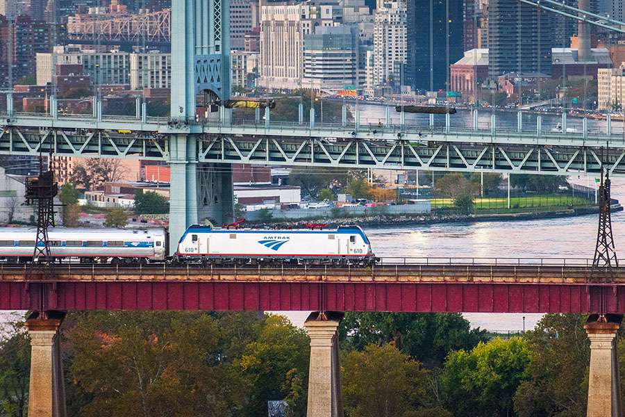 A train travels on a bridge with New York's skyline in the background 