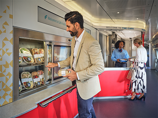 A passenger grabs an item from a refrigerator in the train cafe car.