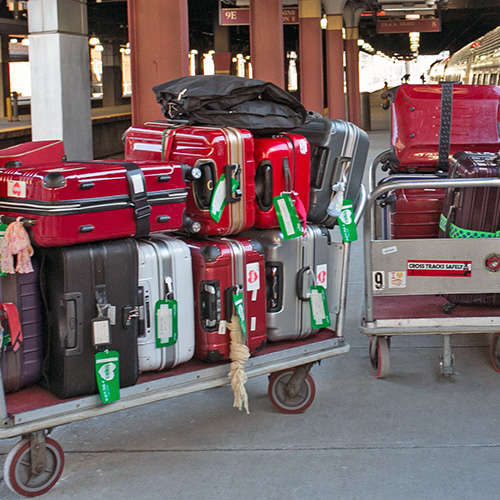 Stack of baggage on a cart on a train platform.