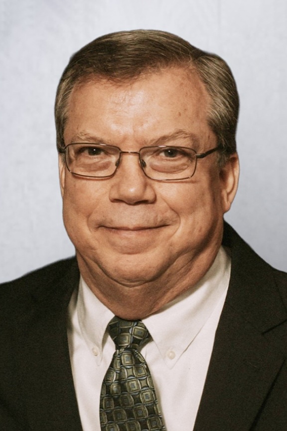 A man in a suit and tie gently smiles toward the camera.