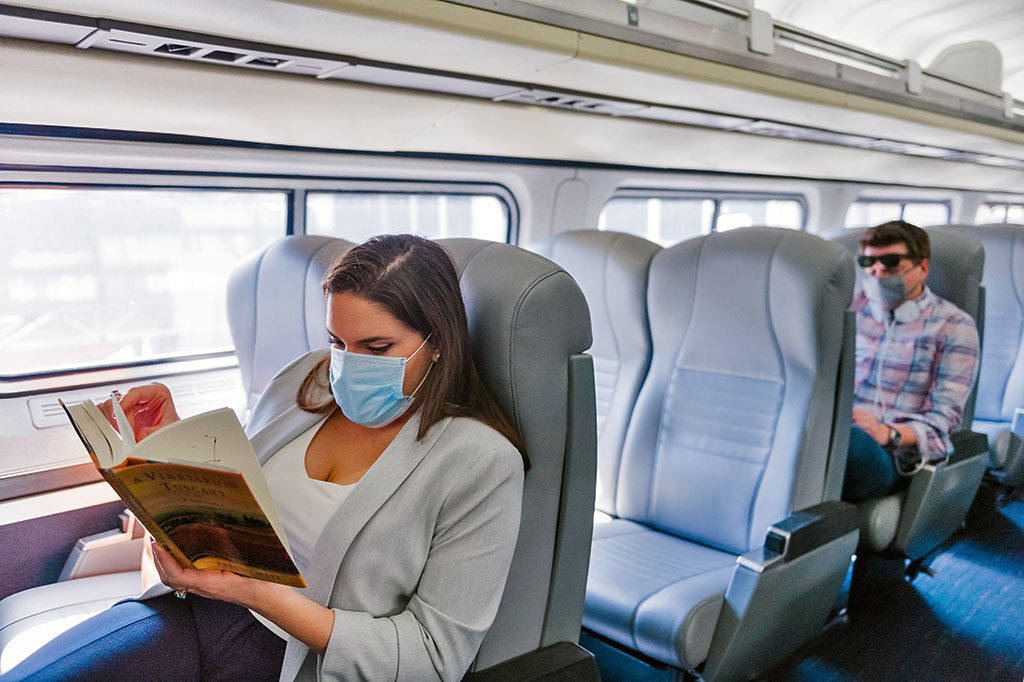Passenger wearing face covering reading book on train.
