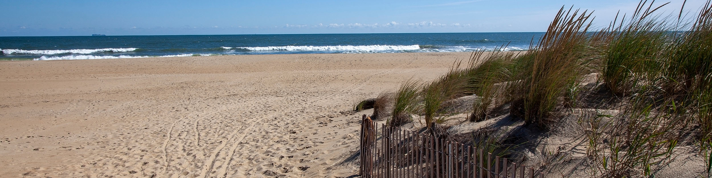 A blue sky shines over the sand and water of Virginia Beach.