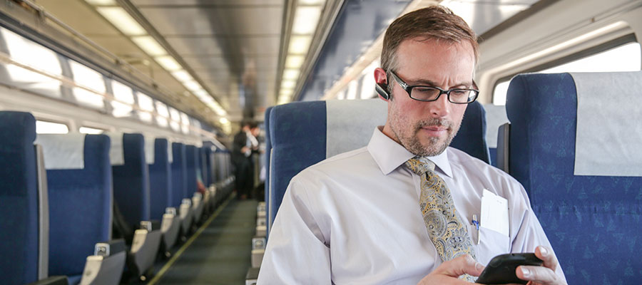 A man in a shirt and tie sits in a train car while on his phone.