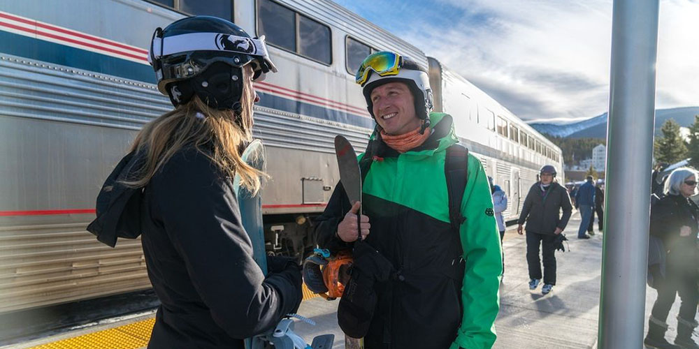 Two people on Amtrak train boarding platform with snow gear ready for skiing and snowboarding