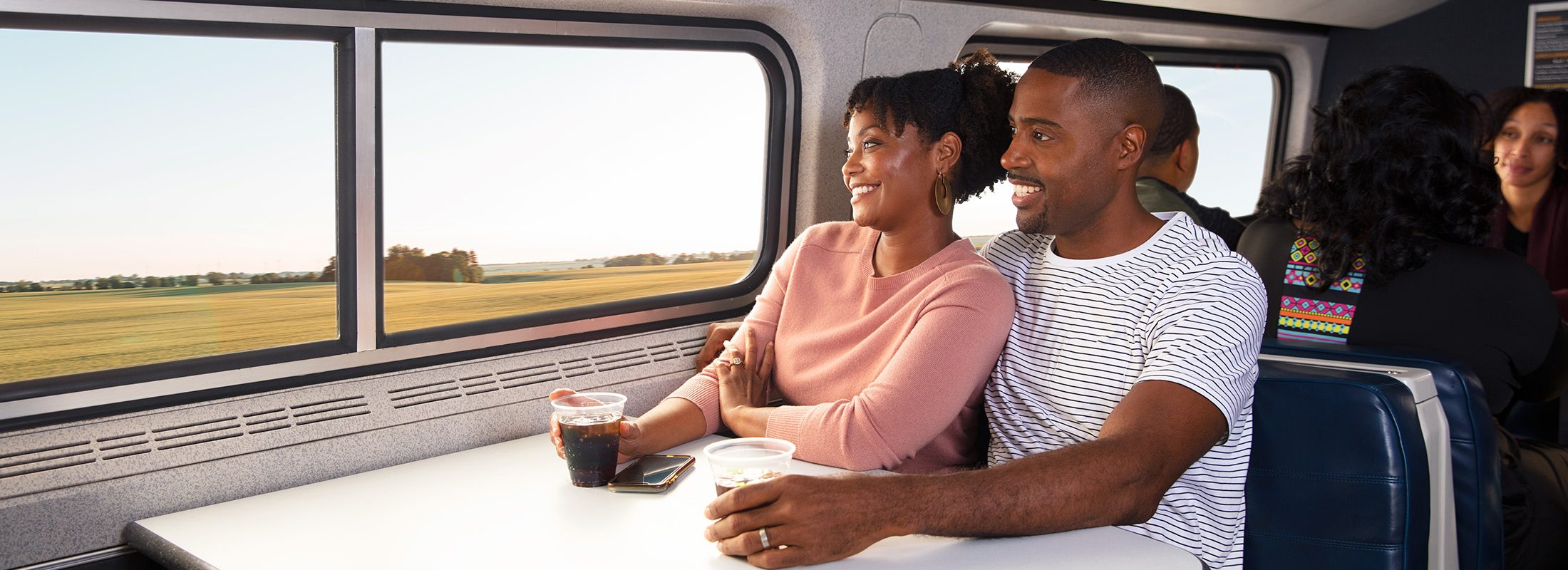 Pareja a bordo del tren mirando por la ventana mientras disfrutan de refrescos