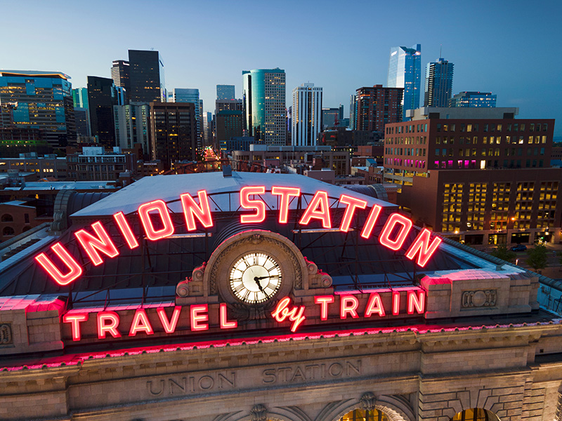 Union Station train station travel by train neon sign with clock and cityscape backdrop in Denver Colorado