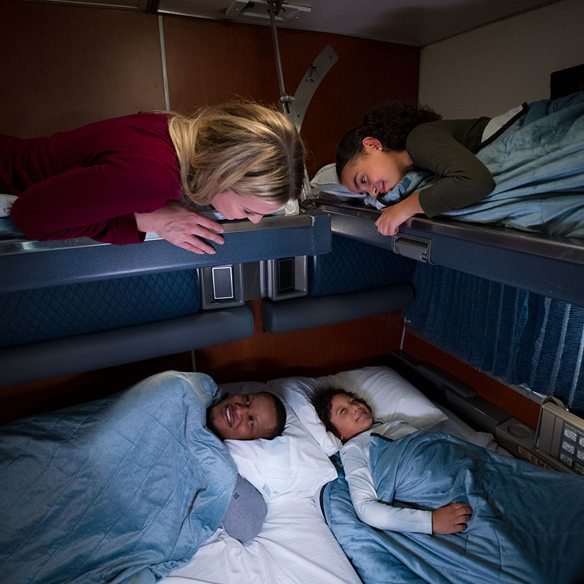 Une famille diversifiée se sourit sur des lits d’une chambre familiale